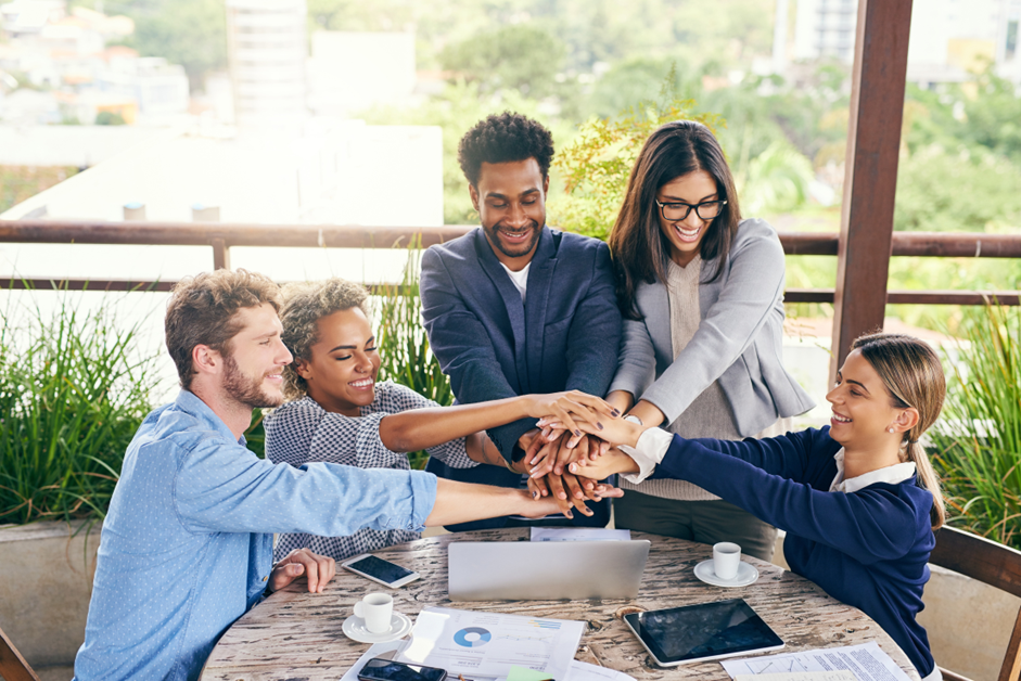 Smiling diverse group of employees high-fiving in a bright modern office, symbolizing teamwork and positive morale.